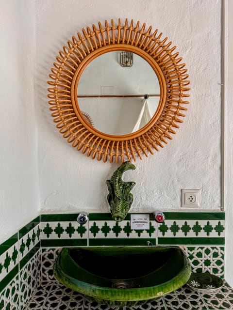A rattan mirror above a green-tiled basin in the Molino Escamillos apartment at Molino del Carmen, Gaucín